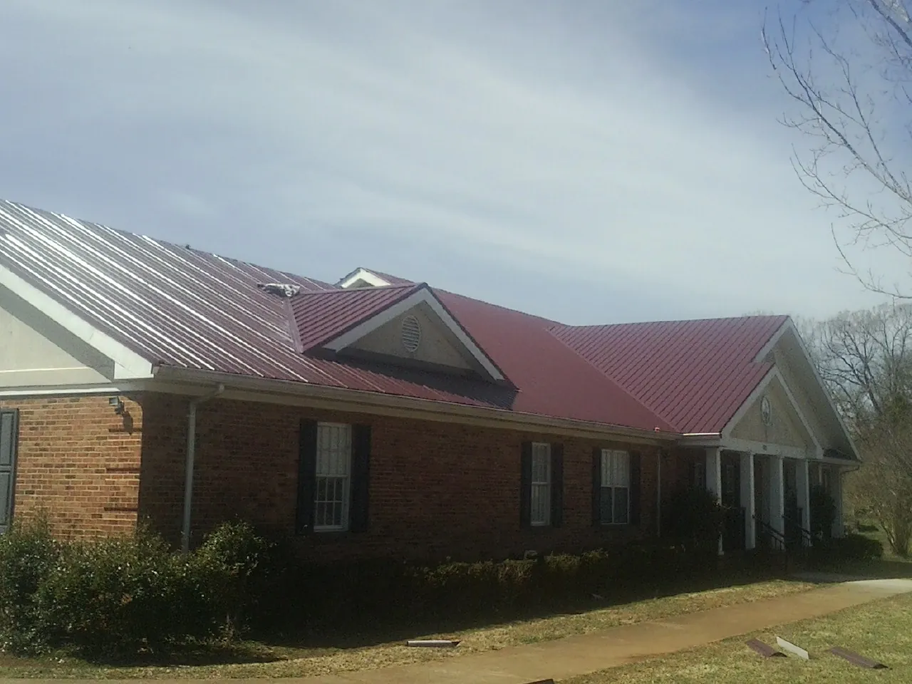 Red metal roof with gabled entries on a long brick building, from a Hail Damage Roof Repair job in Lewisberry