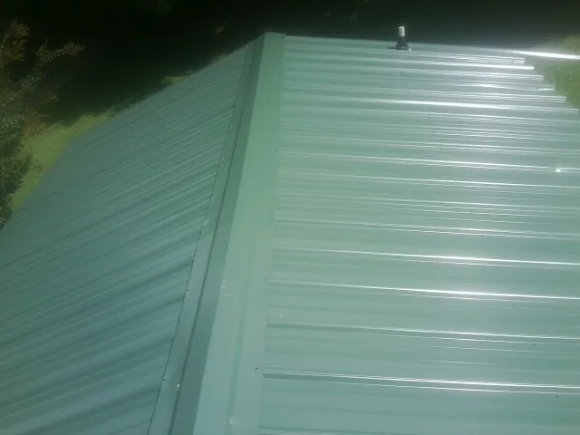 New green metal panels meeting at the ridge of a roof — Flat Roof Repair work by our crew in Lewisberry