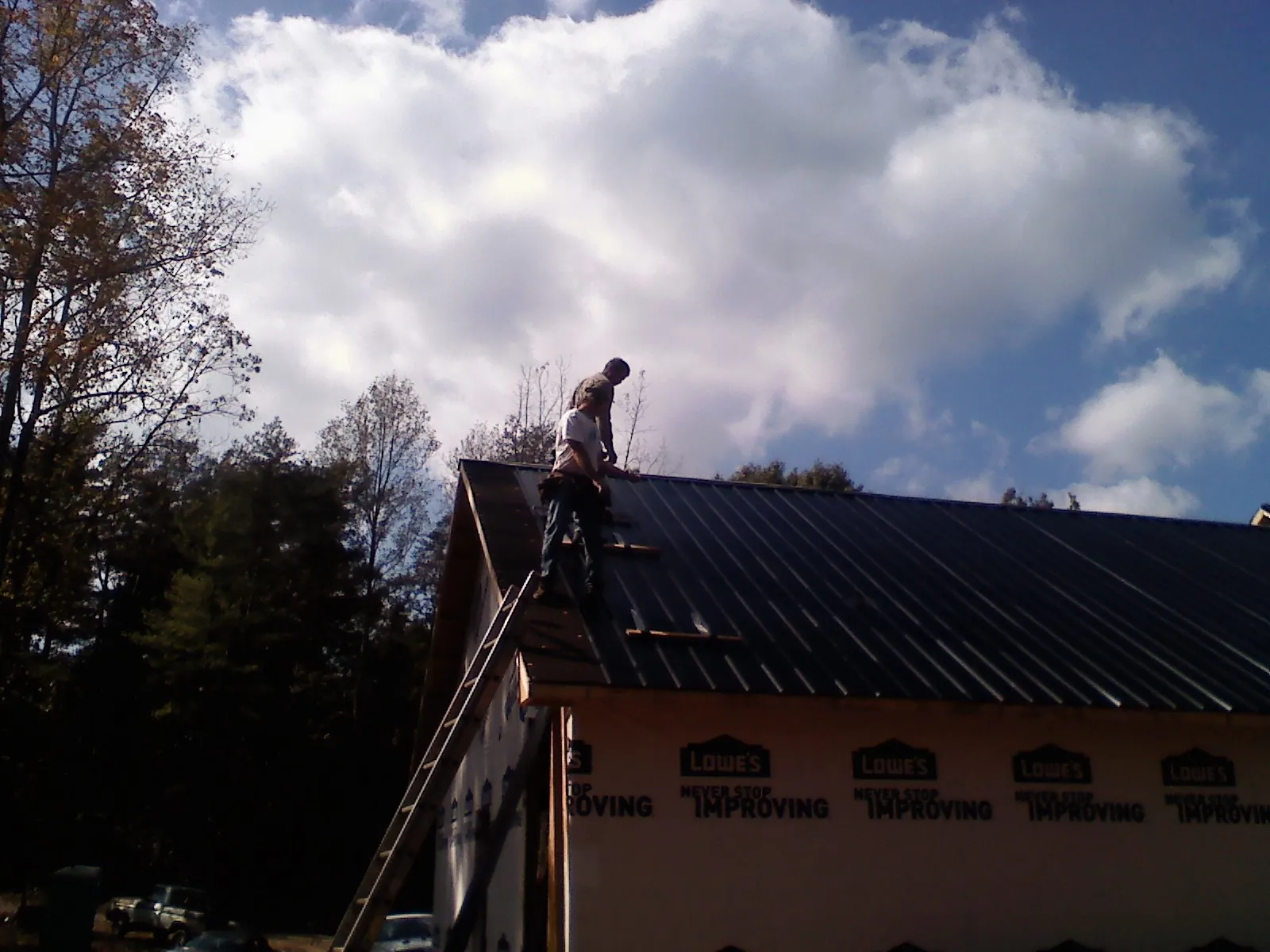 Roofer fastening dark metal panels high against a cloudy sky, from a Roof Inspection job in Lewisberry