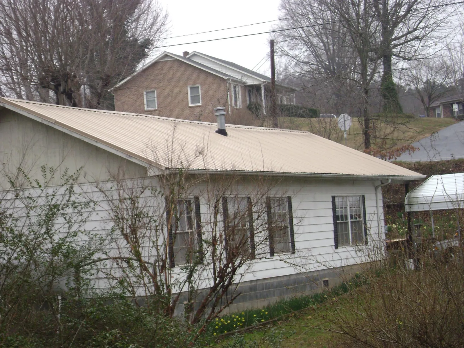 Tan metal roof on a white sided house set into a hillside — Commercial Roofing by Roofing Brothers in Lewisberry